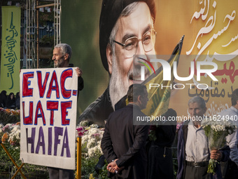 An elderly Iranian protester holds an anti-Israeli placard while standing in front of a giant banner depicting a portrait of Lebanon's Hezbo...