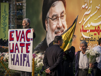 An elderly Iranian protester holds an anti-Israeli placard while standing in front of a giant banner depicting a portrait of Lebanon's Hezbo...