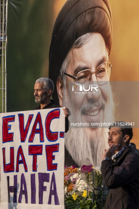 An elderly Iranian protester holds an anti-Israeli placard while standing in front of a giant banner depicting a portrait of Lebanon's Hezbo...