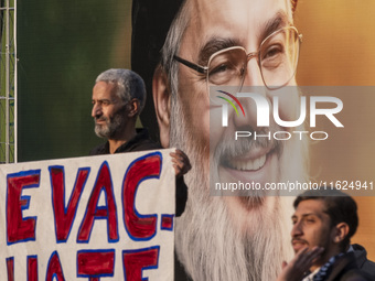 An elderly Iranian protester holds an anti-Israeli placard while standing in front of a giant banner depicting a portrait of Lebanon's Hezbo...