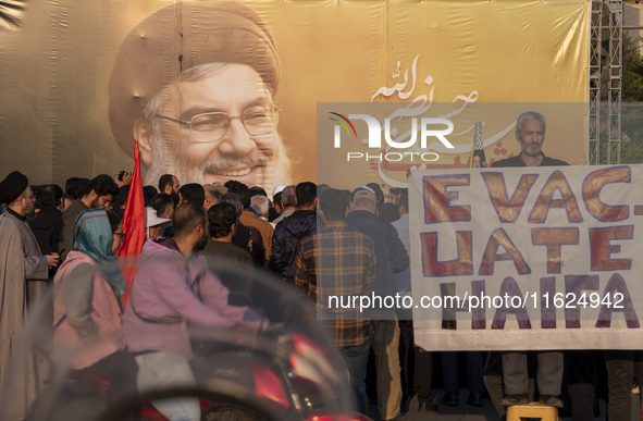 An elderly Iranian protester holds an anti-Israeli placard while standing in front of a giant banner depicting a portrait of Lebanon's Hezbo...