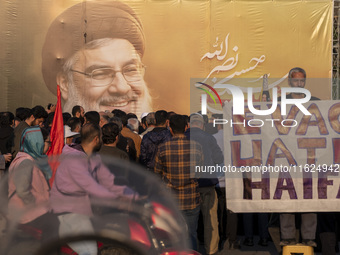 An elderly Iranian protester holds an anti-Israeli placard while standing in front of a giant banner depicting a portrait of Lebanon's Hezbo...