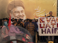 An elderly Iranian protester holds an anti-Israeli placard while standing in front of a giant banner depicting a portrait of Lebanon's Hezbo...