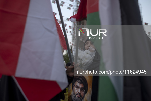 A veiled Iranian protester holds flowers and a portrait of Lebanon's Hezbollah Secretary General, Hassan Nasrallah, while standing behind a...