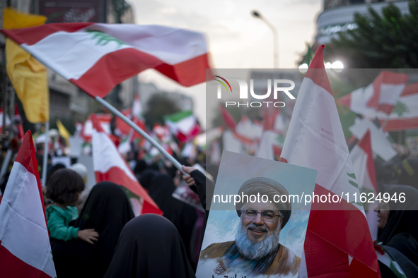 A veiled Iranian protester waves a Lebanese flag while standing behind a portrait of Lebanon's Hezbollah Secretary General, Hassan Nasrallah...