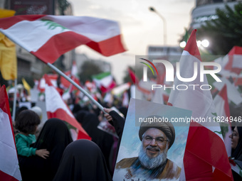 A veiled Iranian protester waves a Lebanese flag while standing behind a portrait of Lebanon's Hezbollah Secretary General, Hassan Nasrallah...