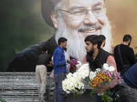 An Iranian protester holds flowers while standing in front of a giant banner depicting a portrait of Lebanon's Hezbollah Secretary General,...