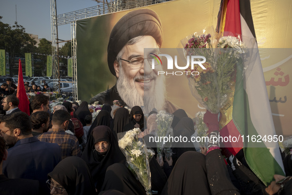 Iranian protesters carry flowers while standing in front of a giant banner depicting a portrait of Lebanon's Hezbollah Secretary General, Ha...