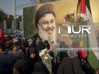 Iranian protesters carry flowers while standing in front of a giant banner depicting a portrait of Lebanon's Hezbollah Secretary General, Ha...