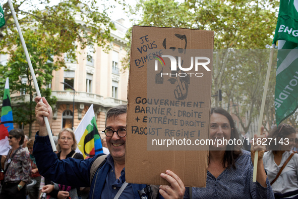 A protester holds a cardboard sign depicting Macron and reading 'I screw you' and 'Barnier government: right and far right'. Between 3,000 a...