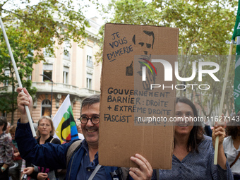 A protester holds a cardboard sign depicting Macron and reading 'I screw you' and 'Barnier government: right and far right'. Between 3,000 a...