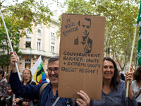 A protester holds a cardboard sign depicting Macron and reading 'I screw you' and 'Barnier government: right and far right'. Between 3,000 a...