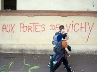 Youths walk in front of graffiti reading 'at the doors of Vichy'. Vichy is the only far-right government in France during WWII. Between 3,00...