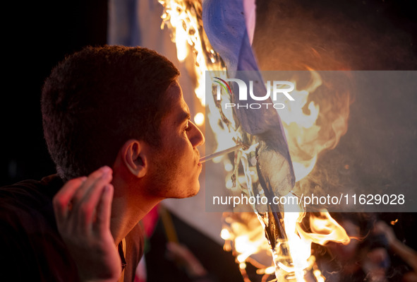 An Iranian man lights a cigarette using a burning Israeli flag while celebrating Iran's missile attack against Israel in Tehran, Iran, on Oc...