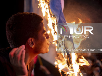 An Iranian man lights a cigarette using a burning Israeli flag while celebrating Iran's missile attack against Israel in Tehran, Iran, on Oc...