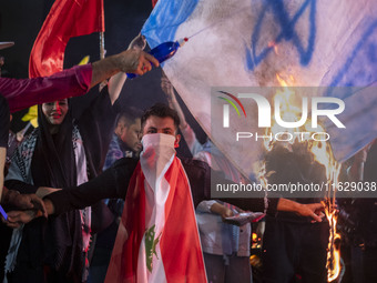 An Iranian man wears a Lebanese flag while protesters burn an Israeli flag during a celebration for Iran's missile attack against Israel in...