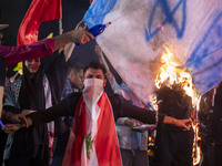 An Iranian man wears a Lebanese flag while protesters burn an Israeli flag during a celebration for Iran's missile attack against Israel in...