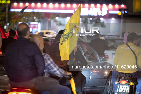 A veiled Iranian woman sits on a motorcycle, carrying a flag of Lebanon's Hezbollah, while celebrating Iran's missile attack against Israel,...