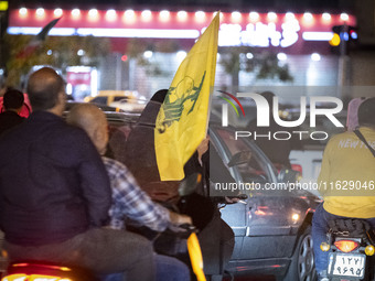 A veiled Iranian woman sits on a motorcycle, carrying a flag of Lebanon's Hezbollah, while celebrating Iran's missile attack against Israel,...