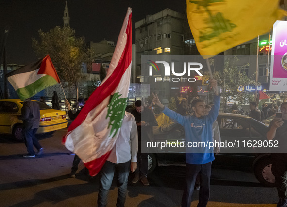 Iranian men wave Lebanon's Hezbollah flag, a Lebanese flag, and a Palestinian flag while celebrating Iran's missile attack against Israel in...