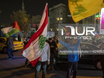 Iranian men wave Lebanon's Hezbollah flag, a Lebanese flag, and a Palestinian flag while celebrating Iran's missile attack against Israel in...