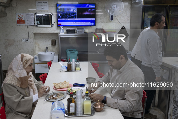 An Iranian couple sits at a small local restaurant while a live report about Iran's missile attack against Israel is broadcast on a televisi...