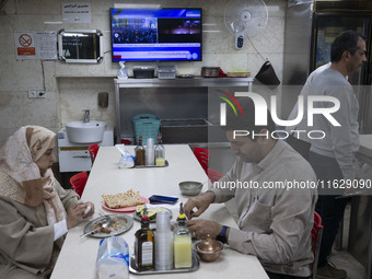 An Iranian couple sits at a small local restaurant while a live report about Iran's missile attack against Israel is broadcast on a televisi...