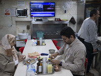 An Iranian couple sits at a small local restaurant while a live report about Iran's missile attack against Israel is broadcast on a televisi...