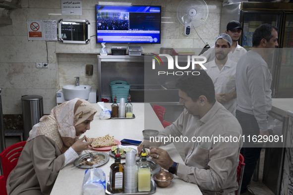 An Iranian couple sits at a small local restaurant while a live report about Iran's missile attack against Israel is broadcast on a televisi...