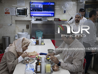 An Iranian couple sits at a small local restaurant while a live report about Iran's missile attack against Israel is broadcast on a televisi...