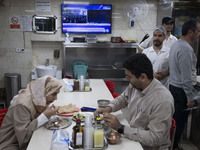 An Iranian couple sits at a small local restaurant while a live report about Iran's missile attack against Israel is broadcast on a televisi...