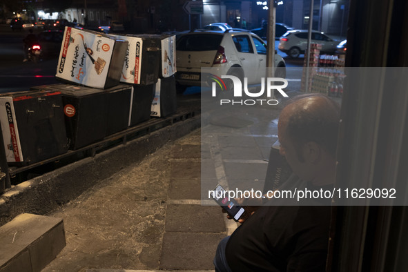 An Iranian man sits on a sidewalk while checking the latest news about Iran's missile attack against Israel in Tehran, Iran, on October 1, 2...