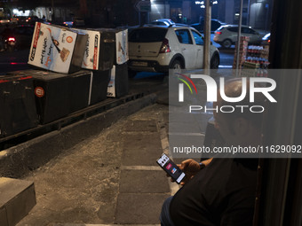 An Iranian man sits on a sidewalk while checking the latest news about Iran's missile attack against Israel in Tehran, Iran, on October 1, 2...