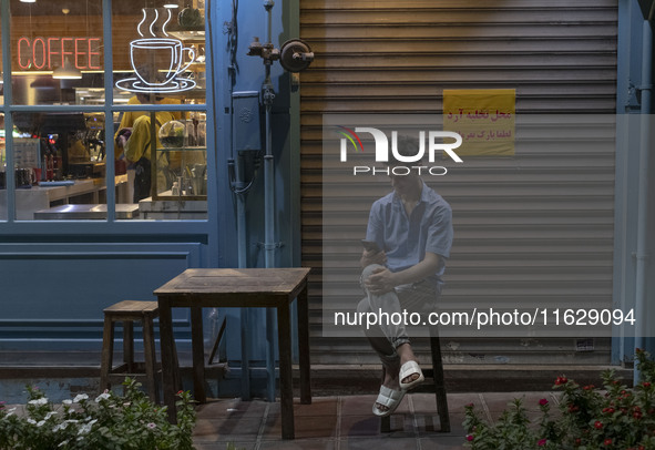 A young Iranian worker sits outside a cafe in downtown Tehran, Iran, on October 1, 2024, while checking the latest news about Iran's missile...