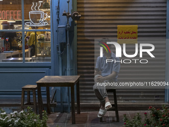 A young Iranian worker sits outside a cafe in downtown Tehran, Iran, on October 1, 2024, while checking the latest news about Iran's missile...