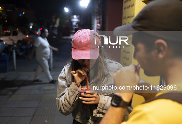 Iranian youths drink fruit juice while standing on a sidewalk in downtown Tehran, Iran, on October 1, 2024, after Iran's missile attack agai...