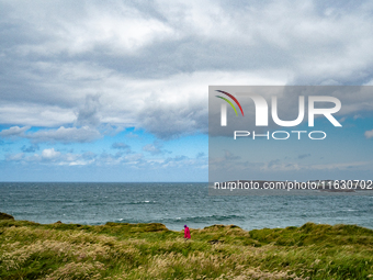 A person walks along the cliffs of the Causeway Coast Area in County Antrim, Northern Ireland, on July 2024. (