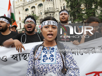 Doctors and citizens hold placards and shout slogans while marching with burning torches during a protest against the rape and murder of a P...