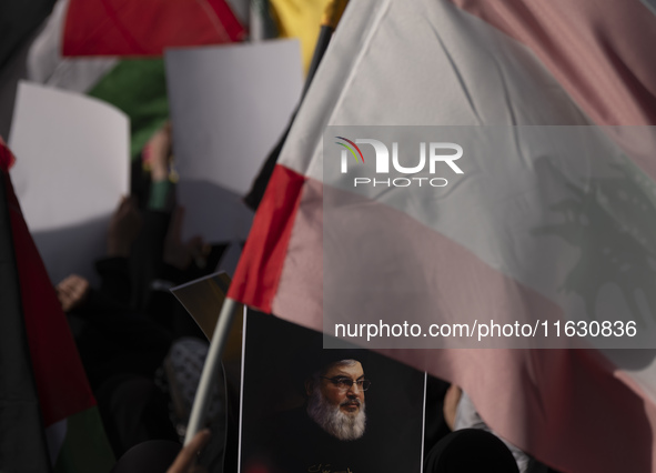 A veiled Iranian woman holds a portrait of Lebanon's Hezbollah Secretary General Hassan Nasrallah under a Lebanese flag during a gathering m...