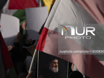 A veiled Iranian woman holds a portrait of Lebanon's Hezbollah Secretary General Hassan Nasrallah under a Lebanese flag during a gathering m...