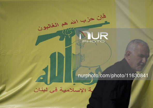 An elderly Iranian man stands in front of a flag of Lebanon's Hezbollah during a gathering marking the memory of Hezbollah Secretary General...