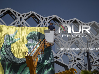 An Iranian worker hangs a banner featuring a portrait of Lebanon's Hezbollah Secretary General Hassan Nasrallah in Tehran, Iran, on October...