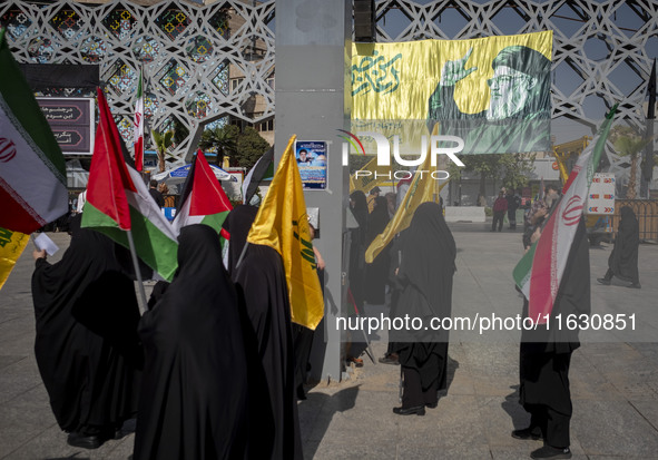 Veiled Iranian women hold an Iranian flag, Palestinian flags, and flags of Lebanon's Hezbollah while standing under a portrait of Hezbollah...