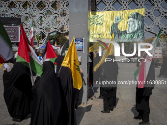 Veiled Iranian women hold an Iranian flag, Palestinian flags, and flags of Lebanon's Hezbollah while standing under a portrait of Hezbollah...