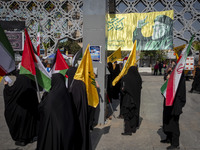 Veiled Iranian women hold an Iranian flag, Palestinian flags, and flags of Lebanon's Hezbollah while standing under a portrait of Hezbollah...