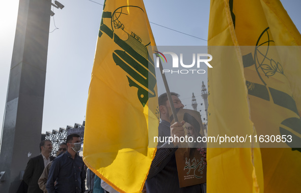 An Iranian man holds a flag of Lebanon's Hezbollah and a portrait of Hezbollah Secretary General Hassan Nasrallah during a gathering marking...