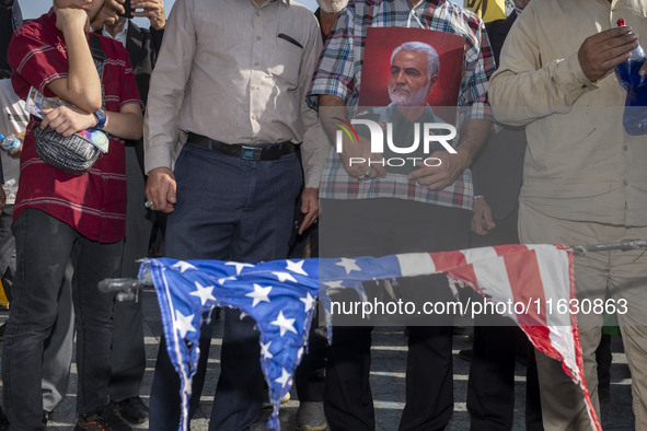 An Iranian man holds a portrait of former commander of IRGC's Quds Force, General Qassem Soleimani, while standing behind a burnt U.S. flag...