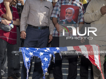 An Iranian man holds a portrait of former commander of IRGC's Quds Force, General Qassem Soleimani, while standing behind a burnt U.S. flag...