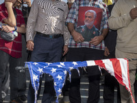 An Iranian man holds a portrait of former commander of IRGC's Quds Force, General Qassem Soleimani, while standing behind a burnt U.S. flag...