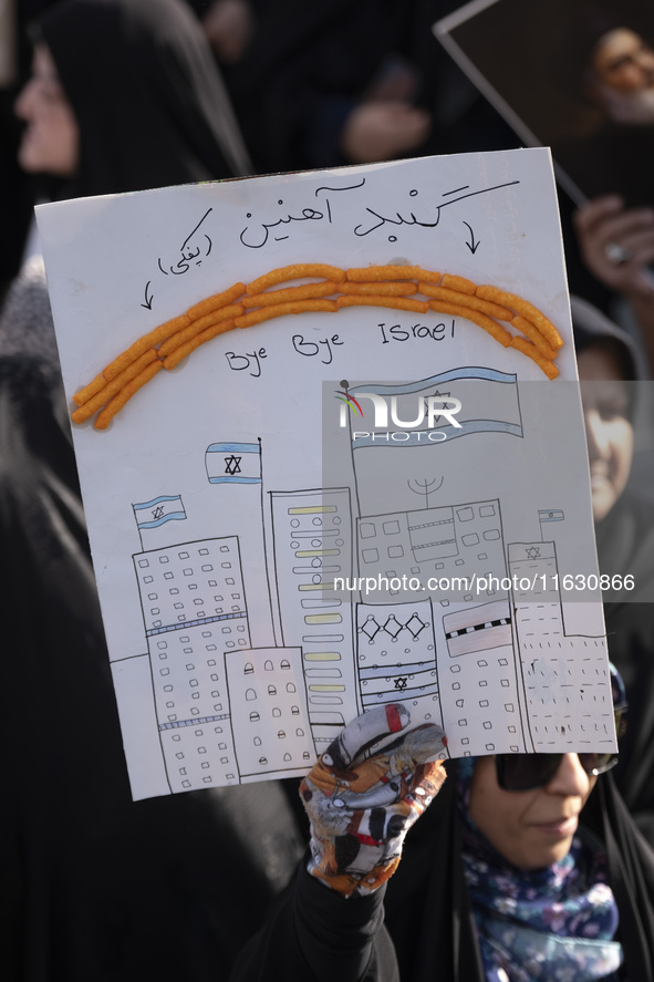 A veiled Iranian woman holds an anti-Israeli placard with snacks pasted on it as a symbol of the Israeli Iron Dome, and a Persian script tha...